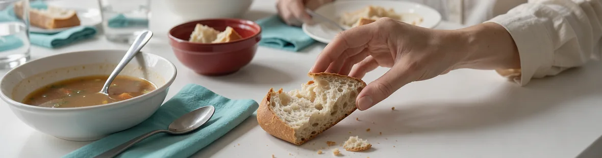 A diner reaches for a torn piece of bread beside bowls of soup during a shared meal at home
